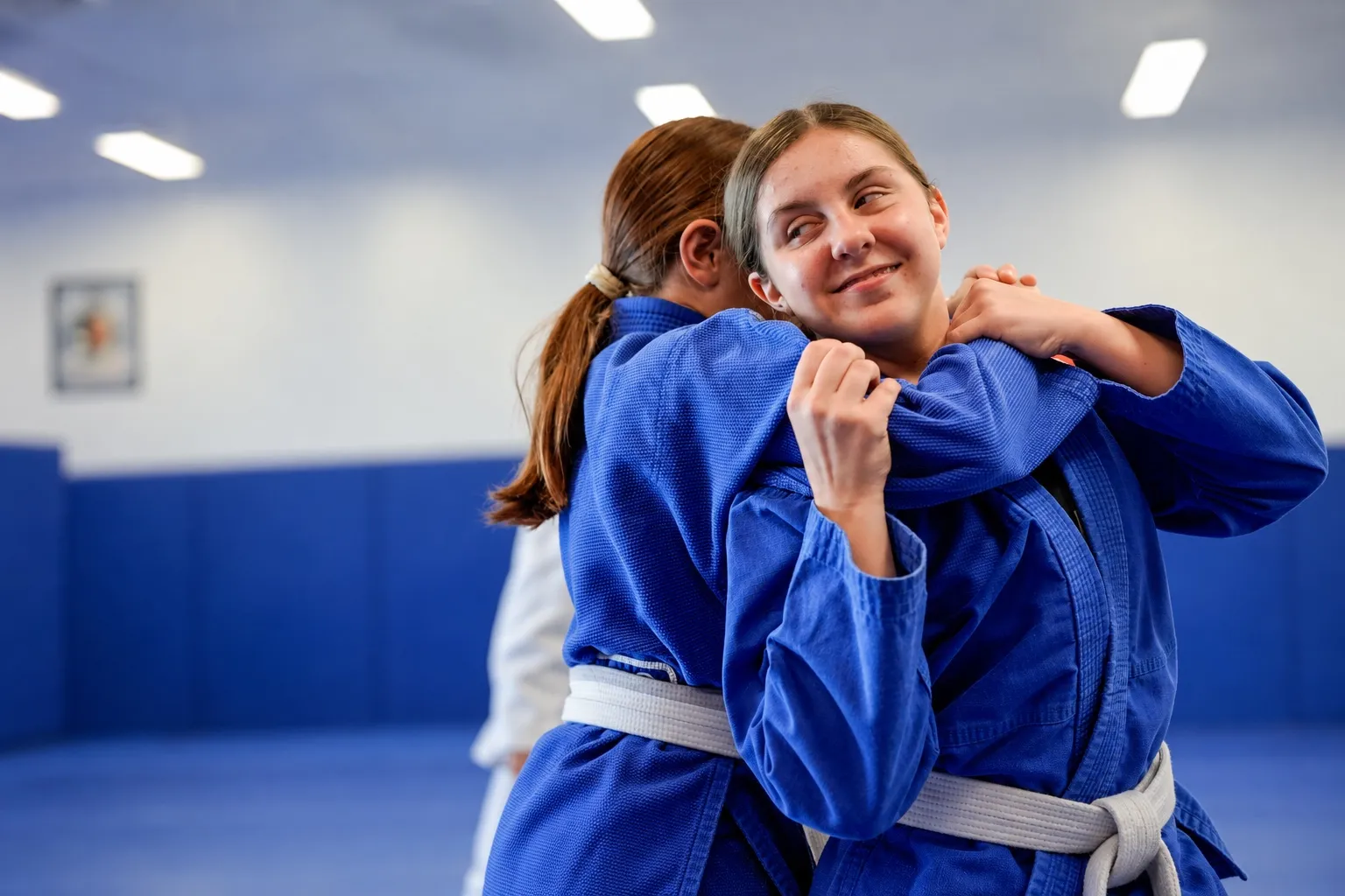 Two teenage girls in blue gis, one smiling at the camera