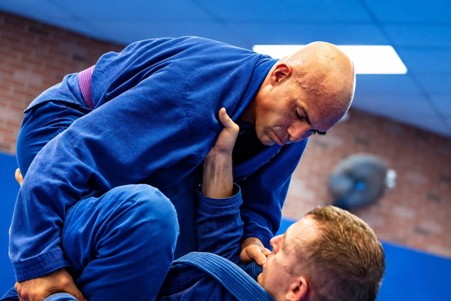 An adult student in a blue gi training with a coach on the mat