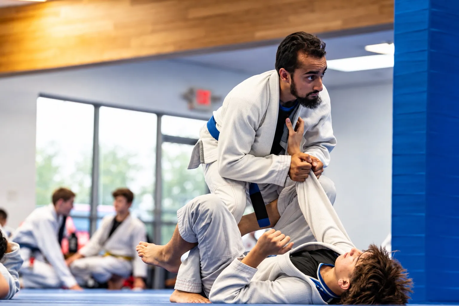 A coach demonstrating a technique on a student while the class watches by the windows